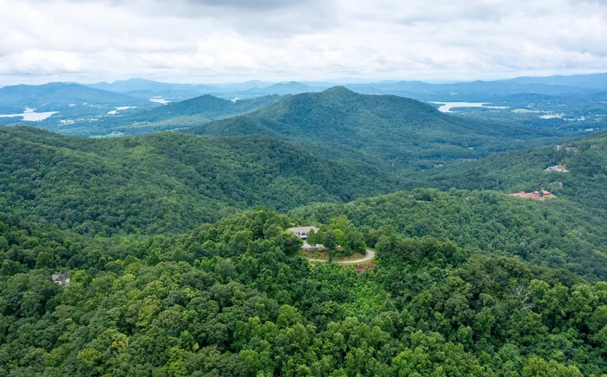 A scenic overlook featuring rolling hills, dense forests, and a winding road—inviting guests to venture out for hiking, nature photography, or simply soaking in the tranquil surroundings. The view hints at the local attractions like Hamilton Gardens, trails, and Lake Chatuge.