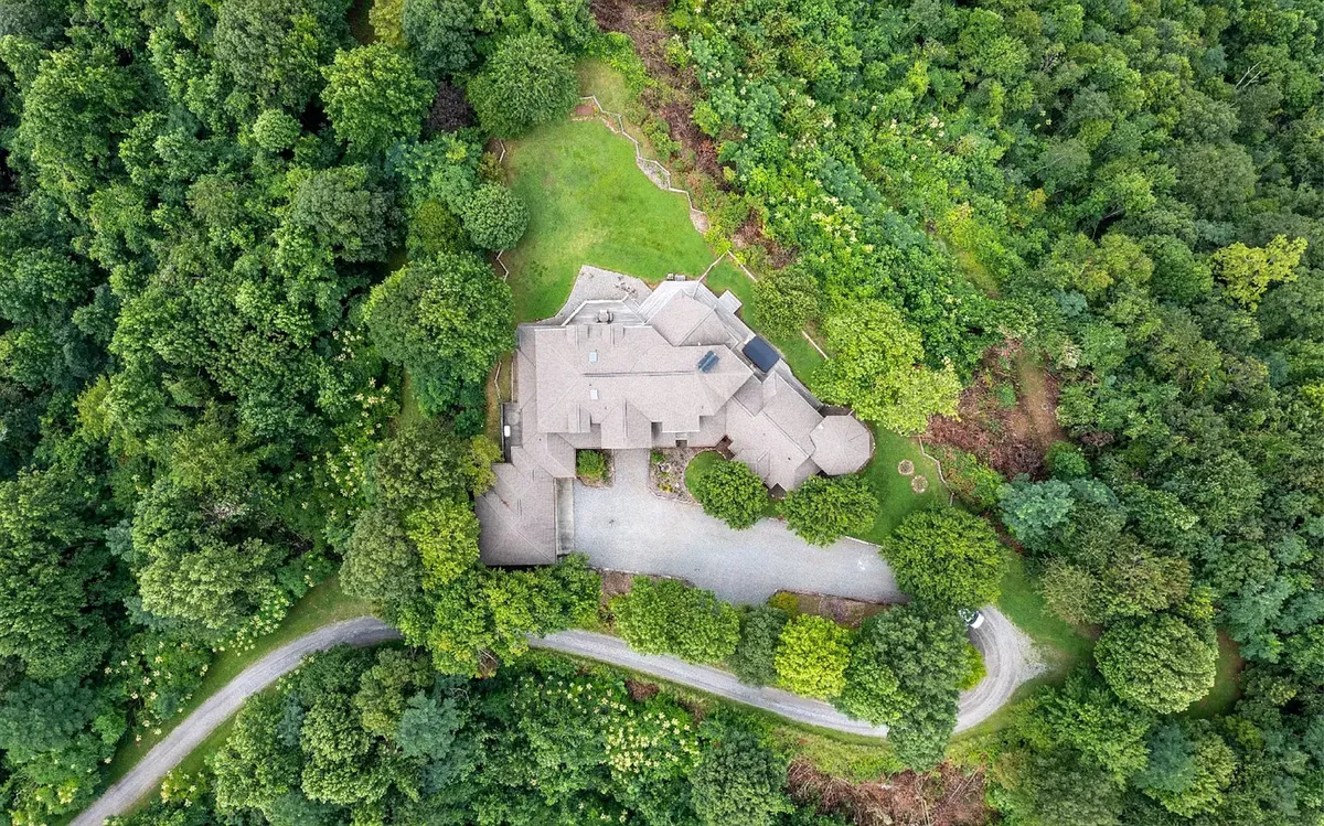 A wide shot of the house set against lush greenery, with a winding driveway and plenty of space for outdoor exploration. The grounds suggest opportunities for activities like nature walks, gardening, and wildlife watching, and the peaceful, inviting mood reinforces the sense of adventure and togetherness.