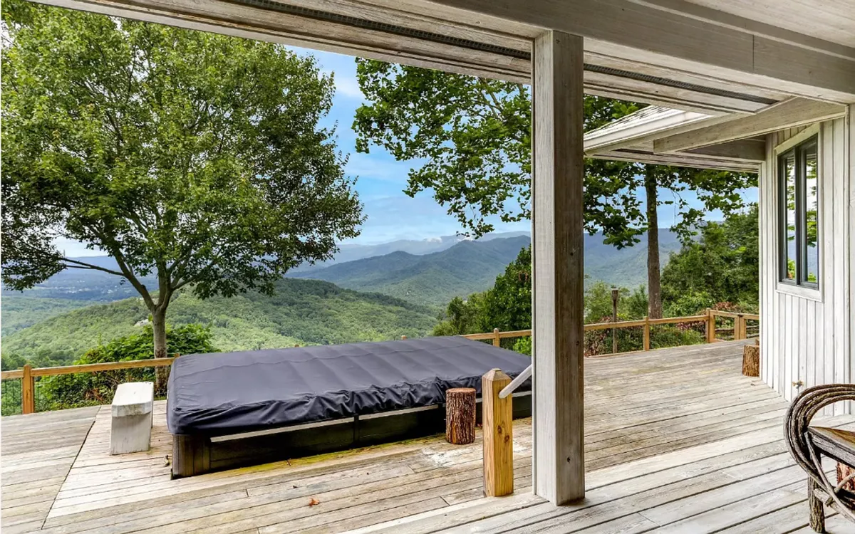 An expansive deck with a comfortable lounge and dining area, partially covered for year-round enjoyment, overlooks sweeping mountain vistas. The scene is set for relaxation, outdoor dining, and stargazing, with soft lighting that enhances the peaceful ambiance as day transitions to night.