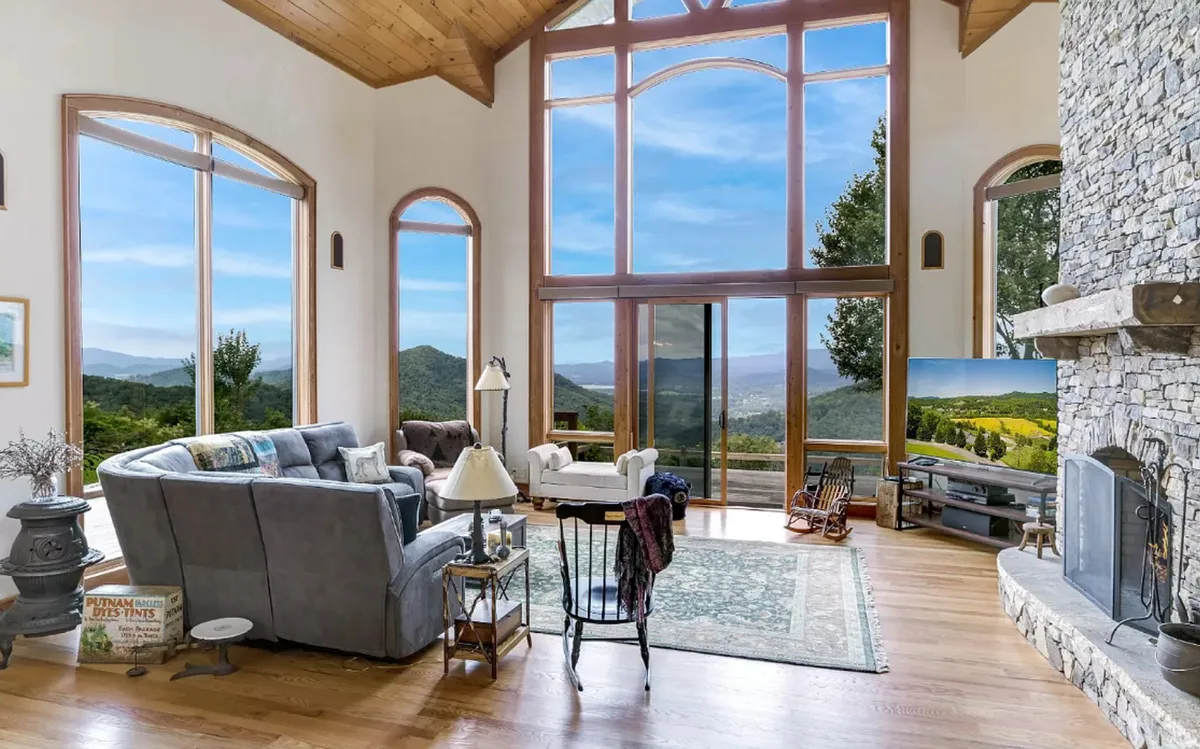 A cozy yet spacious seating area featuring a large stone fireplace, comfortable sofas, and floor-to-ceiling windows that look out onto mountain vistas. The space exudes both tranquility and sophistication, ideal for fireside chats or watching sunsets with loved ones.