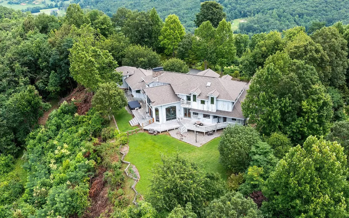 This image captures the house from an exterior angle, enveloped by mature trees and featuring a spacious deck area. The setting suggests ample opportunities for outdoor gatherings, relaxation, and immersing oneself in the natural beauty of the landscape.