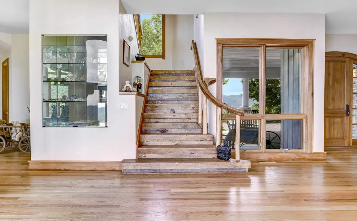 This image captures the entryway of the home, featuring a sturdy wooden door, a prominent staircase, and expansive windows that welcome natural light. The scene offers a sense of arrival and first impressions, hinting at both the privacy and adventure that come with reaching this estate.
