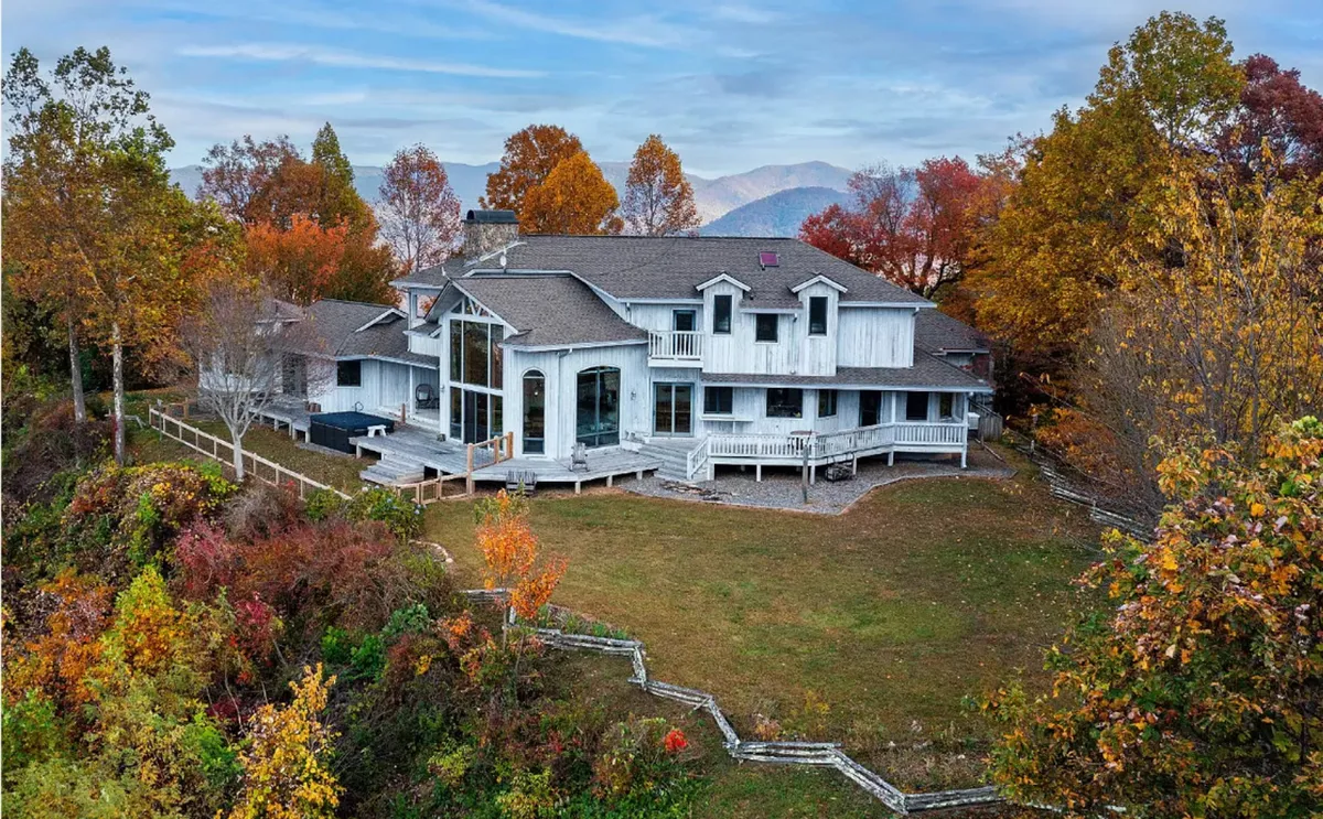 The spacious deck of the estate is highlighted here, surrounded by autumn foliage and framed by large windows that invite the outdoors in. The setting is perfect for outdoor gatherings or intimate moments while watching the sunset, encapsulating the cozy yet scenic atmosphere.